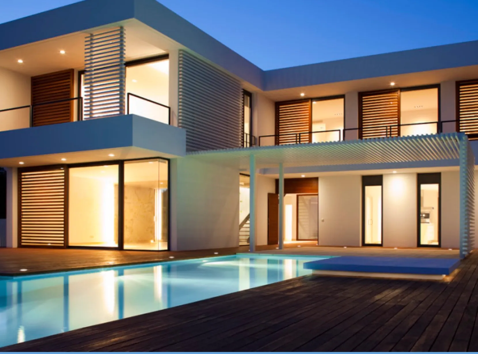 A luxurious modern house featuring large windows, wooden slatted screens, a deck, and an illuminated swimming pool at twilight.